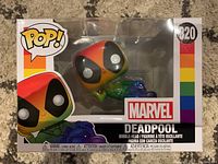 Photo of sealed Deadpool Funko Pop! boxed figure with rainbow color scheme, showing front and top window box design with number 320.