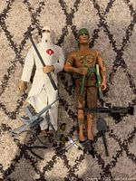 Both GI Joe collectibles, Cobra soldier on left, native warrior on right, with accessories arranged in front.
