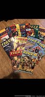 Photo of eleven Tiger Annual comic books, dated 1962-1967, 1969-1970, 1973, 1975-1976, fanned out to display colorful covers featuring motorbikes, animals, soldiers, and sports scenes.