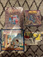 Four comic and graphic novels laid out on carpet. Front covers visible: Excalibur Weird War III, Masters of the Universe, Penguin Dreams and Other Stories, Bizarro comic.