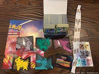 Photo showing a box filled with hundreds of assorted Pokemon trading cards, Eeveelutions lenticular display pieces, part of the Pokemon TCG poster, and sticker sheet.