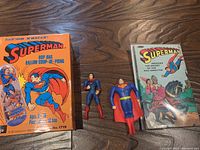 Image displays two Superman action figures, a vintage Superman comic book, and an empty decorative box with Superman graphics.