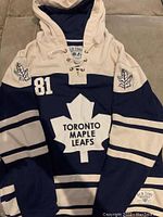 Front view of the navy blue and cream Toronto Maple Leafs hoodie with large maple leaf and team name on front, lace-up collar.