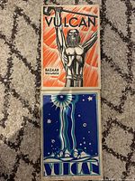 Two Vulcan publications stacked, showing different cover arts: one orange/black with hammer-wielding figure, the other blue with starry night and village