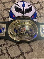 WWE Intercontinental Champion Belt with Rey Mysterio Jr. mask visible in background lying on carpet.