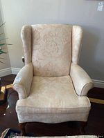 Front view of beige floral patterned upholstered wingback armchair with carved wooden cabriole legs.