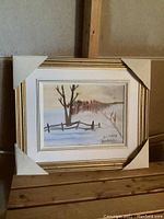 Framed acrylic painting on canvas showing a winter landscape with trees and a fence, framed with white and gold and protected corners.