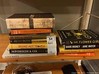 Stack of mixed hardcover and paperback books showing titles such as The Historian, Second Act Trouble, and Dark Money.