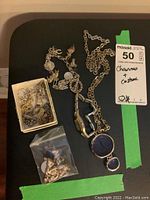 Overview of all items including charm bracelet, small box and plastic bag of charms, necklace, and watch