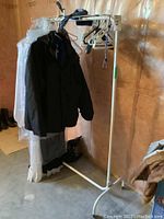 Full view of metal clothing rack with white painted finish, holding a black jacket and garment bags on hangers.