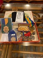 Top view of assorted medals, coins, pins, and cufflinks inside cigar box.