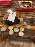 Overview photo showing multiple silver-colored coins spread on a glass surface and a black pouch with coins.