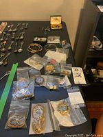 Wide view of the jewelry lot showing bracelets, cufflinks, brooches, earrings, and a decorative bookmark all placed on a black table, some items in plastic bags.