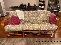 Front view of three-seat rattan sofa with leaf-print cushions and magenta toss pillows