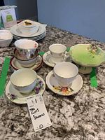 Overview of six vintage tea cups and saucers with various floral patterns and one green pedestal bowl on a granite countertop.