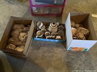 Wide view showing one box with wrapped saucers and one box with teapot and cups, set on concrete floor.