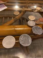 Coins from various countries including Spanish 2 pesetas, Italian 100 lire, Icelandic coins, among others, displayed on a glass surface with part of the pouch visible.