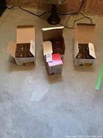 Four boxes of stemless glassware on a concrete floor, three boxes open showing individual glasses inside with cardboard compartments, one box unopened.