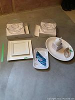 Lot contents with two glass chip and dip bowls in boxes, ceramic platters, honey pot, and plastic party trays arranged on floor.
