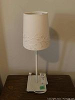 Side view of a bedside lamp with cream-colored fabric shade decorated with floral and branch patterns, mounted on a white metal base.