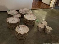 Stacked plates and saucers arranged by type, showing quantity and floral design with gold edges.
