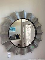 Frontal photo showing the whole round mirror with scalloped grey frame and clear reflection.