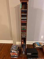 Wooden CD rack loaded with multiple CDs and DVDs, stacked with a few VHS tapes and plastic storage cases nearby.