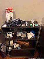Photo shows shelving unit with assortment of items including electronics, personal care items, jewelry, and accessories arranged on three shelves.
