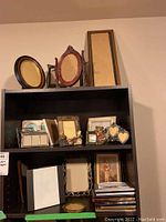 Wide view of shelf with multiple picture frames of various sizes and materials including wood and metal.