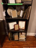 Shelf with assorted picture frames and photo albums, showing various sizes including heart shape and rectangular frames and stacked photo albums