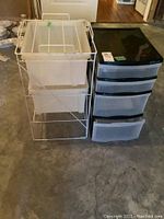 Photo showing black and grey plastic storage drawer unit next to the metal rack with clear plastic bins.