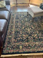 Overall view of the navy blue floral patterned rug placed between a leather couch and ottoman.