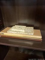 Three rectangular decorative boxes stacked and arranged on a wooden shelf; the largest appears to house the carving set with box showing some damage.