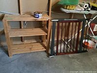 Pine wood utility shelf, wood and metal safety gate, and tub of clothes pins together on basement floor.