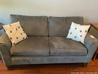 Front view of grey fabric sofa with two cream-colored throw pillows with circular patterns.