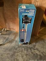 Boxed GSW column sump pump standing on concrete floor, front view of packaging showing pump image and branding.