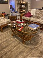 Wide shot showing the rattan coffee table with beveled glass top along with matching end table and rattan sofa in carpeted basement room.