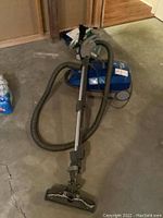 Blue Kenmore canister vacuum with hose, wand, and floor head laying on concrete floor