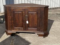 Front view of antique solid wood corner cabinet with two paneled doors and antique metal latch.