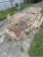 Overall view of vintage oval metal frame table and six chairs on concrete, showing rust and missing table top