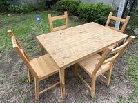 Photo showing the dining table with four wooden chairs arranged around it on grass.
