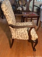 Side view of a vintage wooden armchair with beige and brown patterned upholstery, showing the carved wooden armrest and cabriole front leg.
