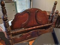 Wooden bed footboard with dark finish, showing detailed carving and turned posts.