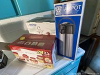 Photo showing boxed Rubbermaid container set, Anchor cake plate in box, and commercial airpot thermos in box on kitchen counter