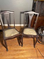 Front view of two mahogany antique dining chairs showing carved backrests, cabriole legs with claw and ball feet, worn fabric seats, and overall condition.