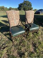 Pair of antique high back chairs set outdoors with tall patterned backs and green leather seats.