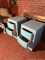 Pair of blue painted solid wood cabinets with three drawers each, shown in front of a brick wall and furniture background. Drawers are open revealing wood interiors.