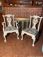 Pair of white Chippendale style chairs, one armchair and one side chair, shown in front of fireplace with detailed carving and patterned cushions.