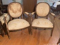 Front view of two chairs showing oval backs, scroll arms, carved wood frames and beige floral upholstery
