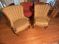 Pair of vintage wingback chairs with beige floral fabric upholstery and wooden legs on hardwood floor